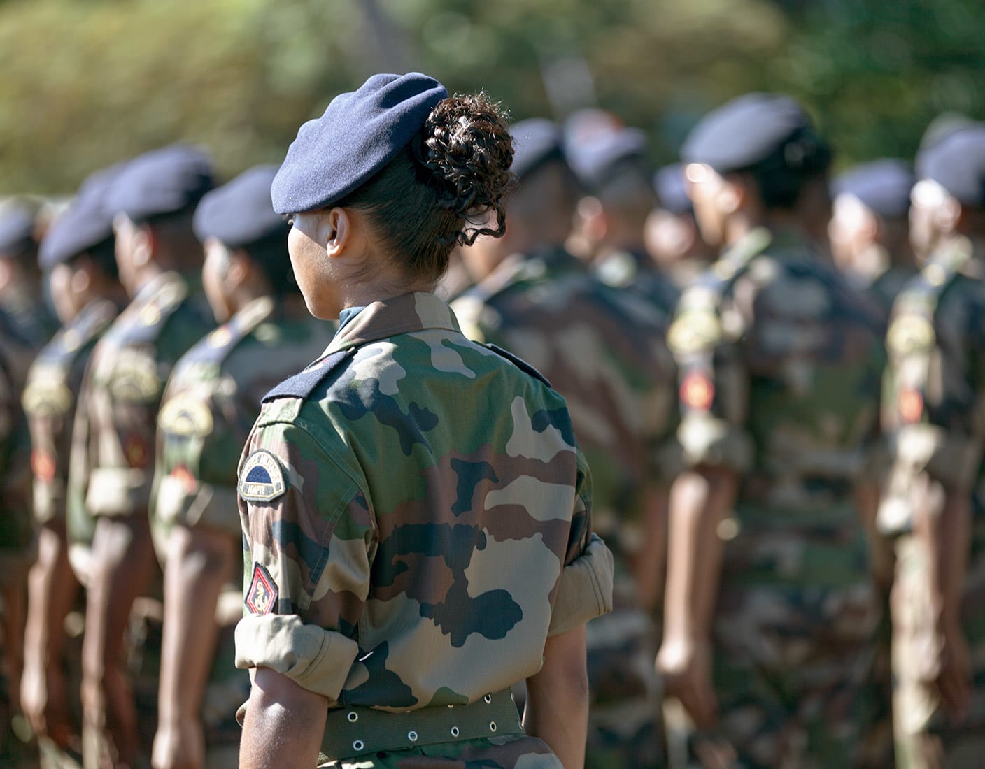 A female officer in military attire stands in front of a group of soldiers.